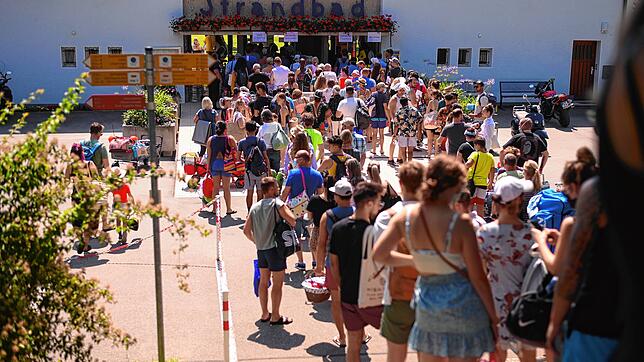 Vor dem Strandbad in Friedrichshafen hat sich vor der Öffnung eine lange Schlange gebildet: Als die Tore aufgehen, teilt sich der Pulk ...