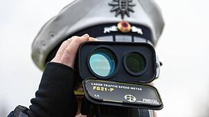 Ein Polizist kontrolliert mit einem Lasermessgerät die Geschwindigkeit der Fahrzeuge.