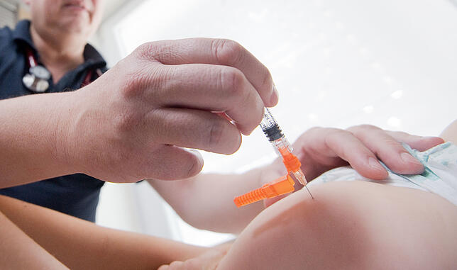 Ein Kinderarzt impft ein einjähriges Kind in den Oberschenkel mit dem Impfstoff Priorix (Lebendvirusimpfstoff gegen Masern, Mumps und ...