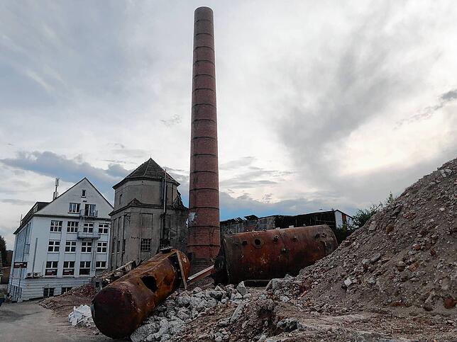 Blick auf das Kesselhaus und den Schornstein Ende Juli 2025: Im Vordergrund zwei verrostete Kessel. Rechts davon der Schutt der bereits ...