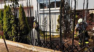 Die Einsatzkräfte der Feuerwehr löschen die Hecke ab, um ein erneutes Aufflammen zu verhindern.