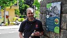 Andreas Bohnenstengel, Chef der Süßmostkelterei Wilhelm Auer, mit Apfelwein am Schild des Heimatpfads der Gemeinde, bei dem die Kelterei ...