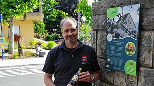 Andreas Bohnenstengel, Chef der Süßmostkelterei Wilhelm Auer, mit Apfelwein am Schild des Heimatpfads der Gemeinde, bei dem die Kelterei ...