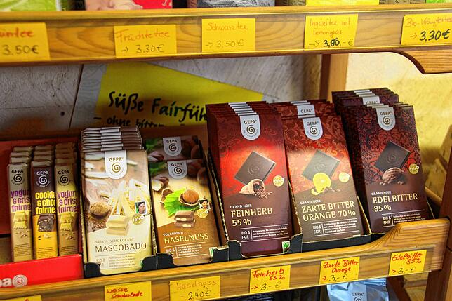 In einem kleinen Regal des Hofladens werden Fairtrade-Lebensmittel wie Schokolade oder Kaffee angeboten.