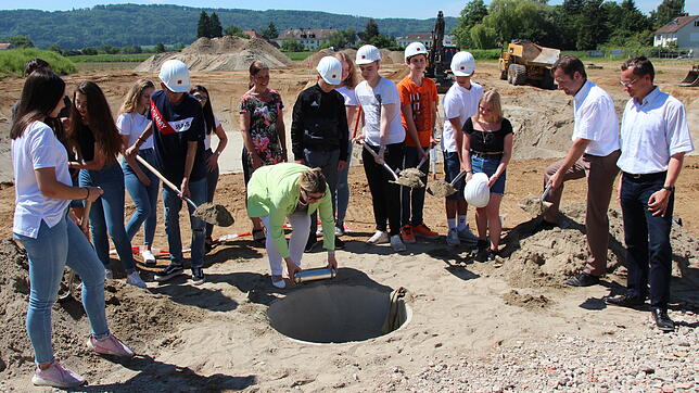 Schulleiterin Cosima Breitkopf legt die Zeitkapsel in das Loch vor der Baugrube der neuen Gottmadinger Schule. Schülerinnen und Schüler, ...