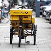 Ein Fahrrad eines Briefträgers steht auf einem Gehweg.