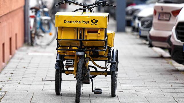 Ein Fahrrad eines Briefträgers steht auf einem Gehweg.