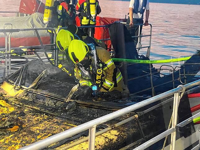 Feuerwehrleute stehen unter schwerem Atemschutz in dem ausgebrannten Motorboot. Es wurde in den Sportboothafen von Unteruhldingen ...