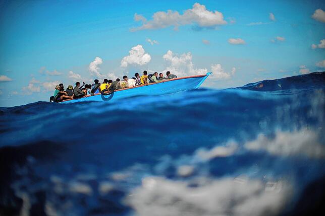 Migranten sitzen in einem Holzboot im Mittelmeer. (Archivbild)