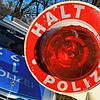 Eine Polizeikelle wird vor ein Polizeiauto gehalten.