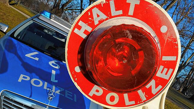Eine Polizeikelle wird vor ein Polizeiauto gehalten.