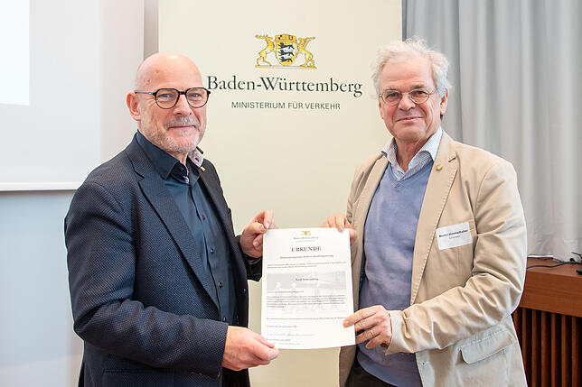 Winfried Hermann übergibt Martin Himmelheber, dem ehrenamtlichen Stellvertreter von Oberbürgermeisterin Dorothee Eisenlohr, die Urkunde ...