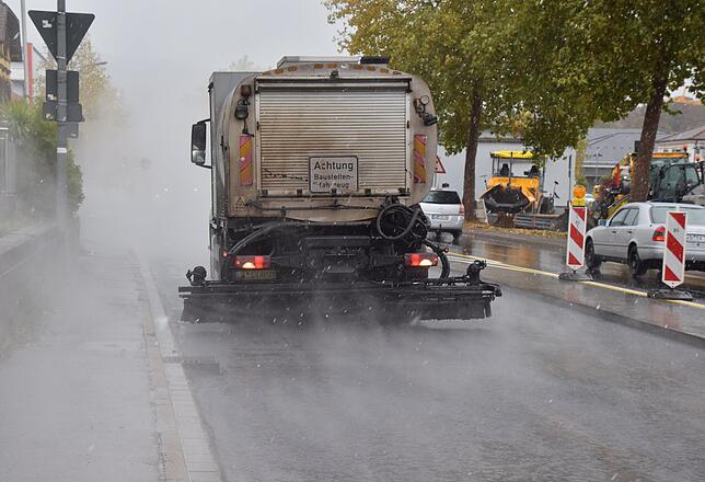 Ein Fahrzeug bringt den speziellen Haftkleber auf, damit sich die Tragschicht gut mit der Binderschicht verbindet. Durch die Nässe von ...