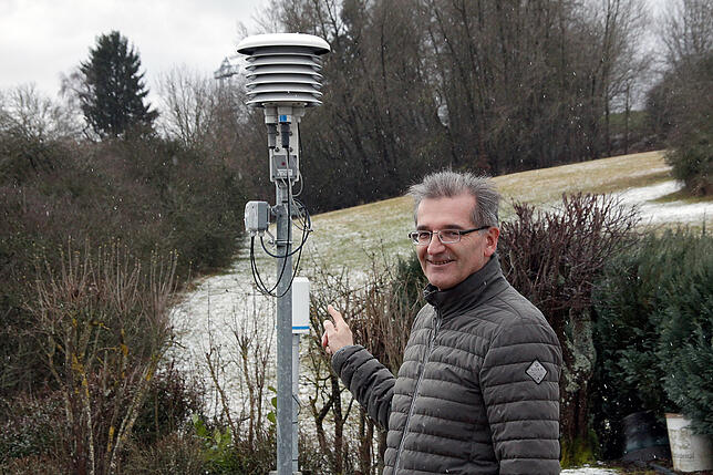 Wolfgang Eich steht vor der Wetterstation des Deutschen Wetterdienstes in seinem Garten. Das Gerät neben ihm misst die Temperatur in ...