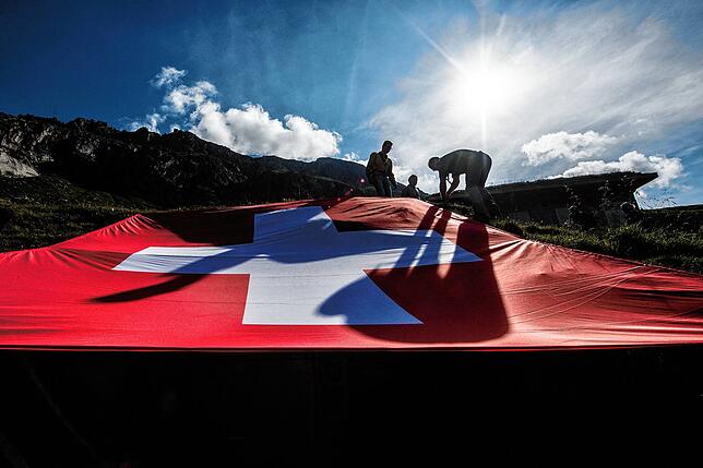 Drei Männer sind am Bundesfeiertag der Schweiz auf dem Gotthard-Pass neben einer großen Schweizerfahne zu sehen. Die Schweiz ist stolz ...