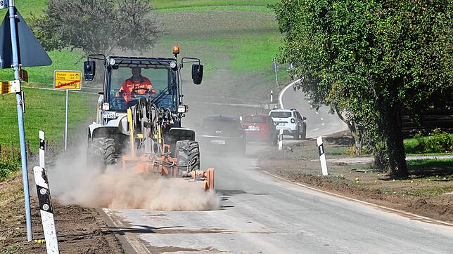 Ein Fahrzeug der Straßenmeisterei wirbelt beim Reinigen des getrockeneten Schlamms ordentlich Staub auf. Der Schlamm kam von einem Feld ...
