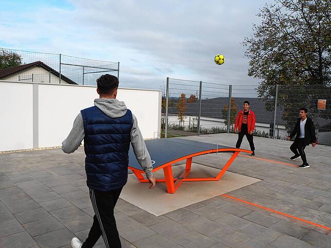 Diese Aufnahme zeigt Jugendliche beim Teqball-Spiel. Es wird mit Fußball über eine gebogene Tischtennisplatte gespielt. Die Sportart ist ...