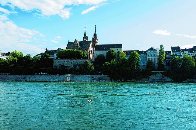 Blick auf Basel und das Münster. Im Vordergrund sind Rheinschwimmer zu sehen.