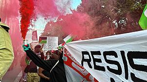 Menschen halten bei einer Pro-Palästina-Demonstration Banner und Flaggen und lassen bunten Rauch aufsteigen auf einer Straße in der ...