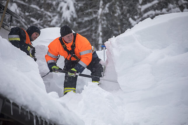 Im bayerischen Buchenhöhe schaufeln Feuerwehrmänner Schnee von einem Dach.
