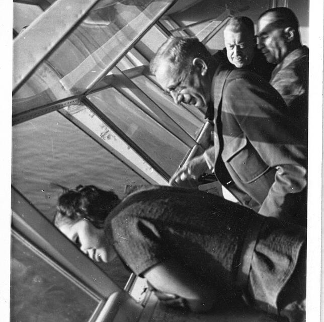 Passagiere blicken aus dem Panoramafenster von LZ 129 „Hindenburg“ auf den Atlantik. Ganz hinten Chef-Luftschiffer Hugo ...