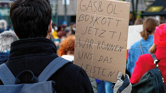 Ein Teilnehmer hält bei einer Demonstration in Köln gegen den Krieg in der Ukraine ein Schild mit Aufschrift &bdquo;Gas und Öl Boykott ...