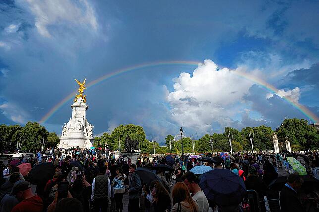 London: Menschen versammeln sich vor dem Buckingham Palast, während ein doppelter Regenbogen am Himmel erscheint.