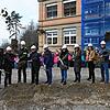 Baubeteiligte und Bürgermeisterin machen den Spatenstich für das Zwischengebäude der Grundschule. Alle Schüler schauen zu.