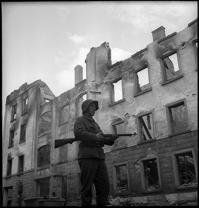 Ein Soldat der Schweizer Armee steht mit seinem Karabiner vor einer ausgeglühten Ruine. Vermutlich um Plünderungen vorzubeugen hat man ...