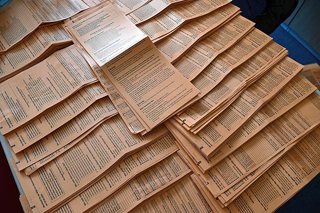 Stapelweise Wahlzettel zum Erfassen liegen auf Tischen im Rathaus.