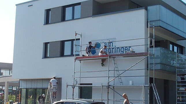 Die Maler legen letzte Hand an und verzieren die Hauswand mit dem Logo "Haus am Teuringer".
