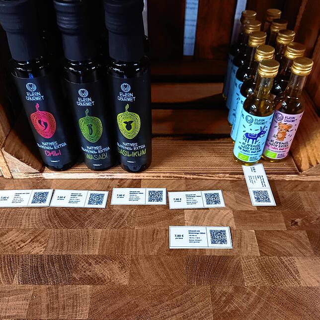 Die Zettel mit den QR-Codes sind hier vor den Flaschen mit Speiseölen aufgereiht.