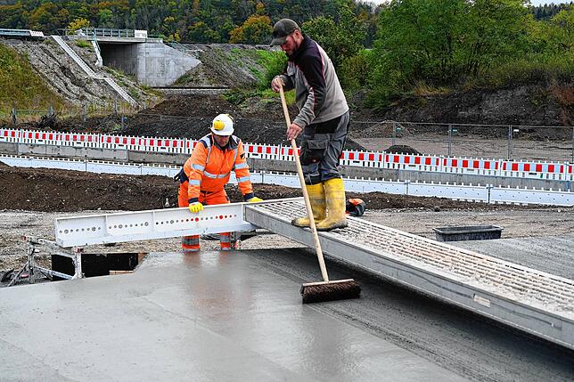 Mit Hilfe eines Straßenbesens wird die notwendige Griffigkeit der späteren Fahrbahnoberfläche in Handarbeit aufgebracht.
