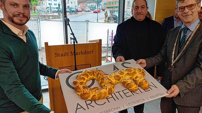 Die Architekten Georg Schmitz und Dietmar Kathan überreichen Bürgermeister Georg Riedmann (von links) einen Hefezopf in Form eines ...