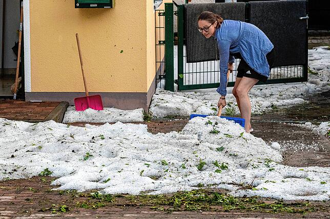 Schnee im Sommer? Eine Frau schaufelt in Bayern nach einem schweren Unwetter Hagelkörner zur Seite.