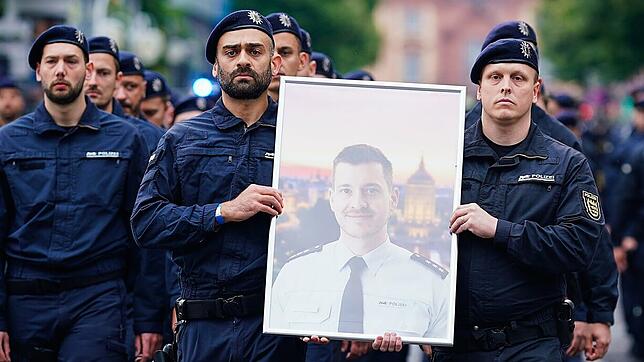 Polizisten tragen bei einem Trauermarsch für den bei einer Messerattacke tödlich verletzten Polizisten Rouven Laur dessen Bild.