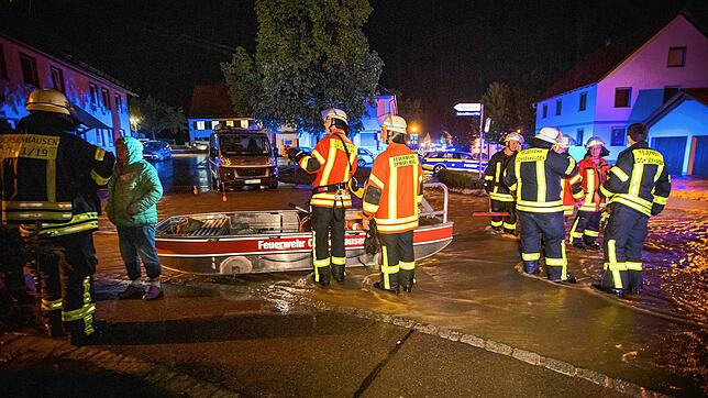 Feuerwehrleute stehen neben einem Feuerwehrboot auf einer Straße in den Fluten eines heftigen Unwetters. Ein Mann war bei den heftigen ...