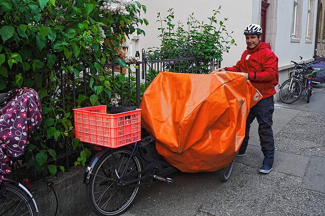 Eine eigens angefertigte Lastwagenplane dient als wetterfeste Abdeckung für das Lastenrad. Jan Otte trägt als Regenschutz Segelkleidung.