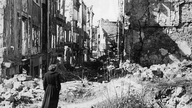Eine Frau geht in einer Straße in Dresden an Häusern vorbei, von denen nach dem Zweiten Weltkrieg nur noch Ruinen geblieben sind. Viele ...