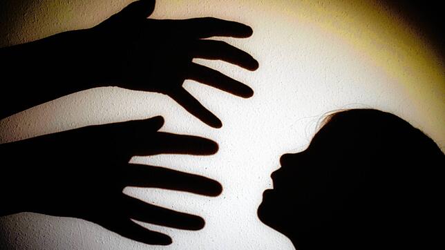 Schatten von Händen einer erwachsenen Person und dem Kopf eines Kindes. (Symbolbild)