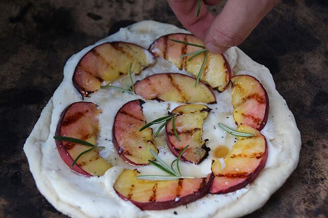 Süße Pizza vom Grill, hier mit vorgegrillten Pfirsichscheiben, gewürzt mit Honig und Rosmarin.