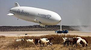 Ziegen grasen vor dem Zeppelin, der an einem Mast in der Sekoma-Salzpfanne der Kalahari-Wüste in Süd-Botswana „geparkt“ schwebt (Foto ...