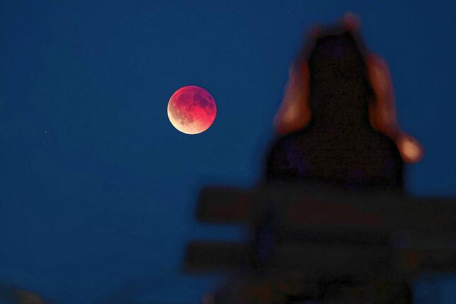 Leipzig: Eine junge Frau betrachtet von einer Parkbank aus die auch als Blutmond bezeichnete totale Mondfinsternis.