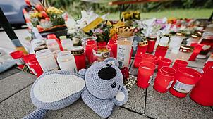 Menschen legen Blumen und Kerzen auf dem abgesperrten Parkplatz in Niedernhall nieder.