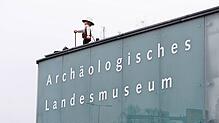 (Archivbild) Das große Playmobilmännchen auf dem Archäologischen Landesmuseum – hier eine Aufnahme von 2023 – blickt in Konstanz auf den ...