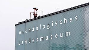 (Archivbild) Das große Playmobilmännchen auf dem Archäologischen Landesmuseum – hier eine Aufnahme von 2023 – blickt in Konstanz auf den ...
