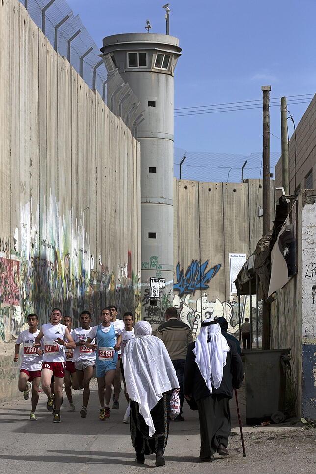 Eine Gruppe Läufer und traditionell gekleidete Palästinenser an der umstrittenen israelischen Trennmauer, in der Stadt Bethlehem im ...