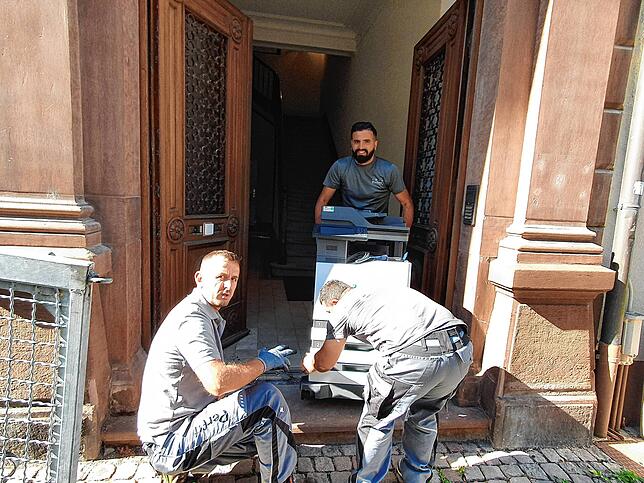 Die Männer packen an – ein großer Drucker wird in die neue Filiale transportiert.