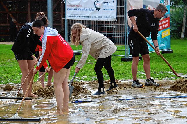 Mit vereinten Kräften schaufeln und rechen viele Helfer die Wassermassen vom Spielfeld.