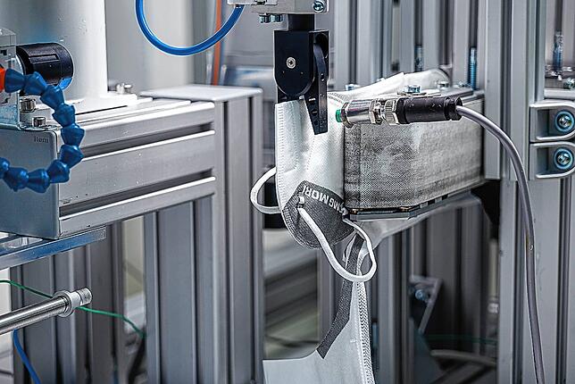 Ein Roboter nimmt die Maske am Ende aus der Maschine und übergibt sie nach einer automatischen Prüfung an die Verpackungseinheit. ...